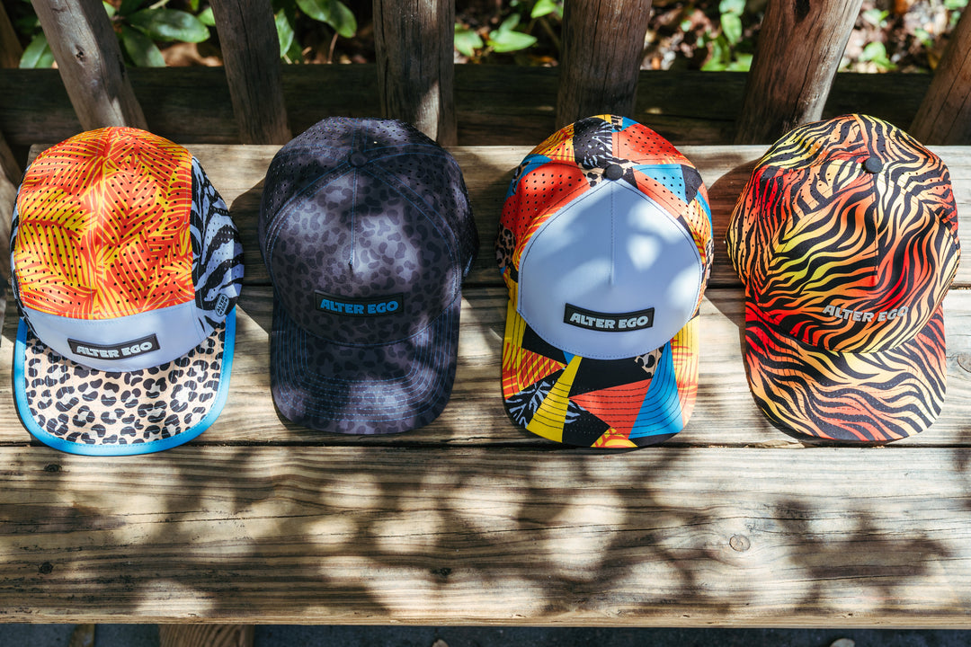 Four colorful patterned Alter Ego performance caps displayed on a wooden bench outdoors.