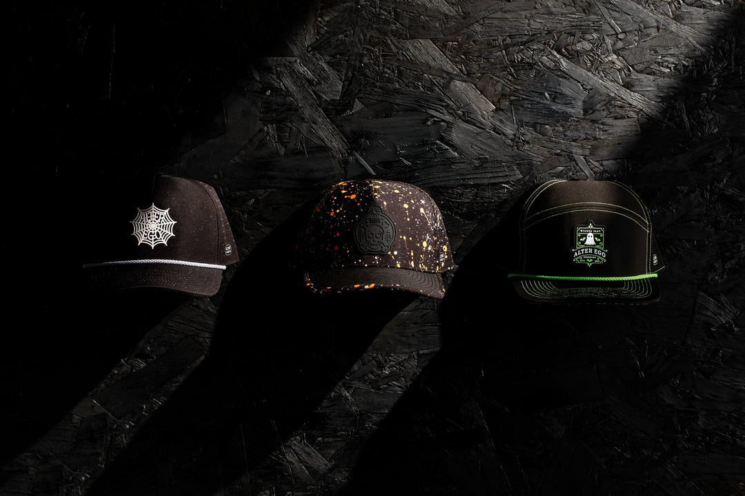 Three Halloween-themed running hats with unique designs: spider web, splattered paint, and Alter Ego logo on a black background