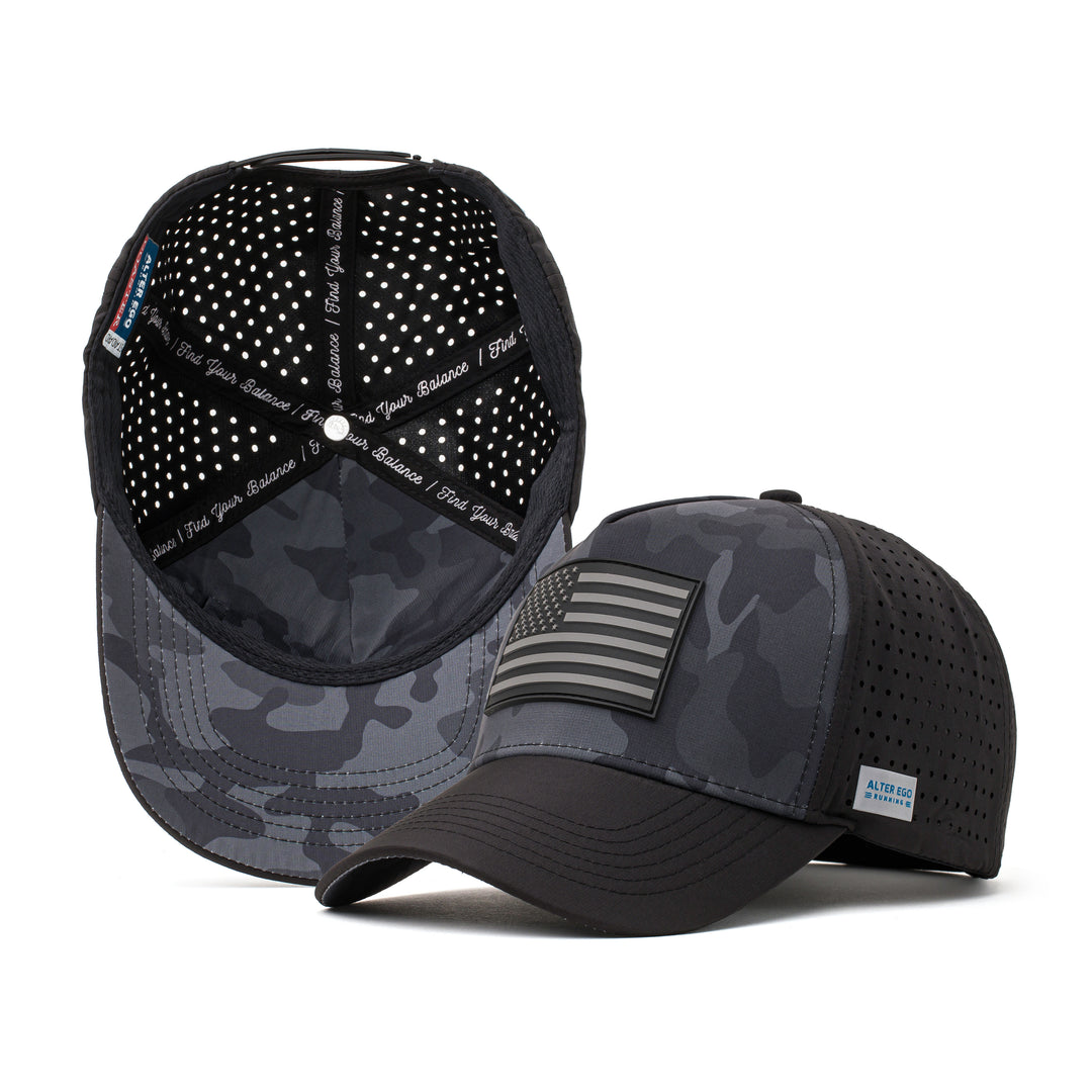 Black performance hat with a dark camo design and a black American flag patch on the front, paired with a breathable perforated mesh back for outdoor and athletic activities.
