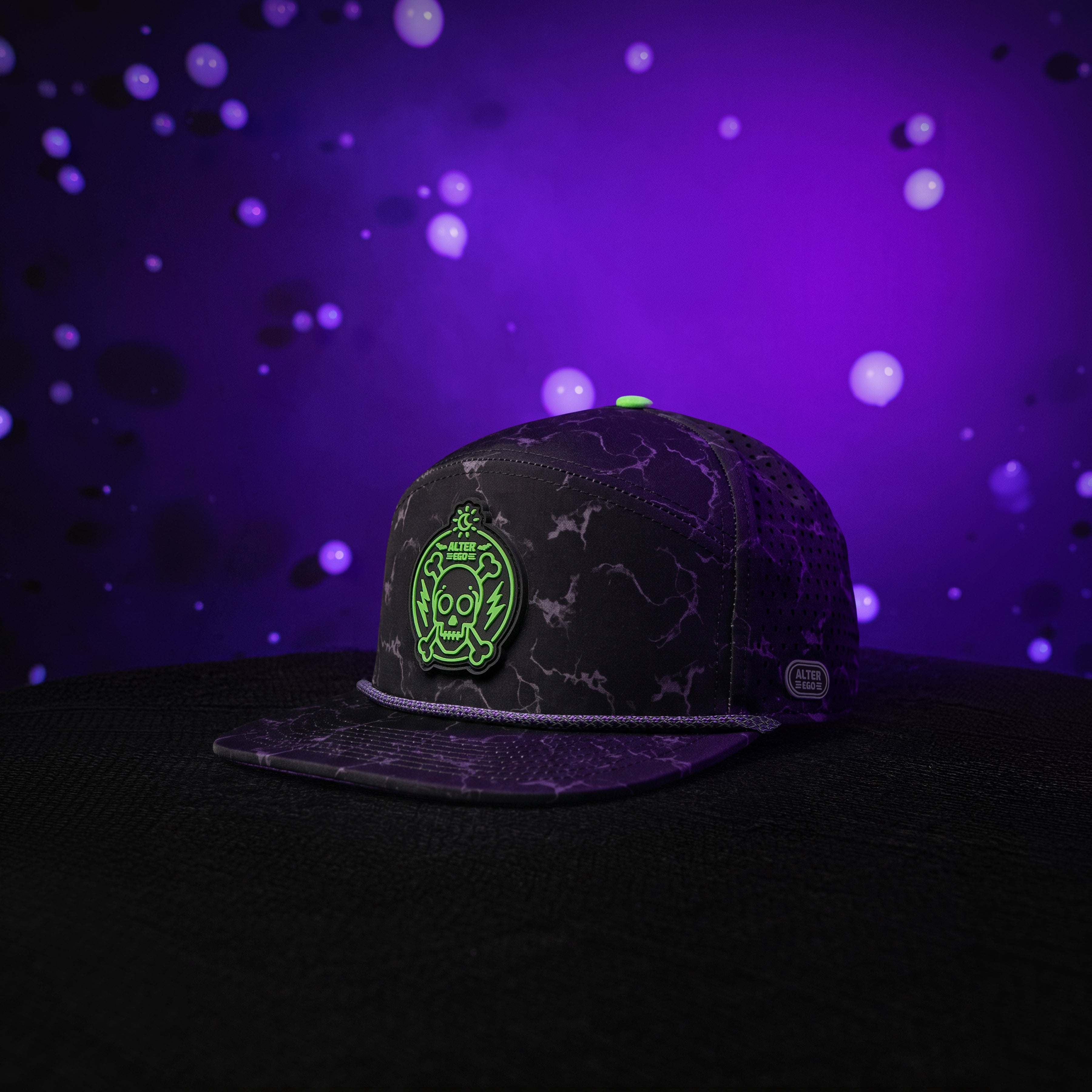Drifter Splash Toxic Storm performance hat with a black lightning pattern, flat bill, neon green skull graphic, and breathable laser-cut side panels against a glowing purple background.